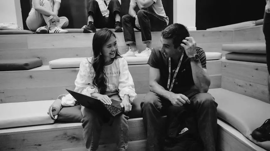 A visiting hiring partner talking with a Challenger on the atrium bleachers at Gauntlet HQ