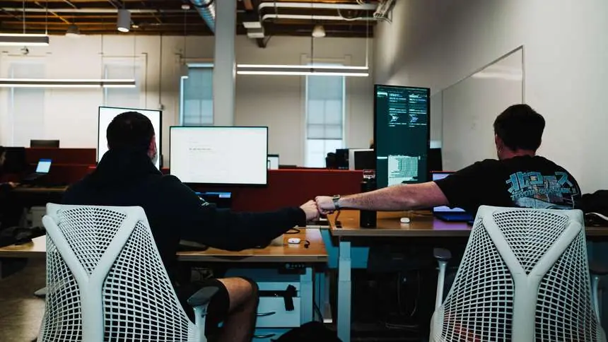 Two Challengers fist bumping across their desks with code on the monitors at Gauntlet HQ